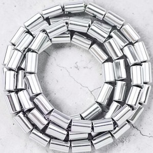 Peut inclure: Un collier composé de nombreux cylindres brillants de couleur argentée. Les perles sont disposées en cercle, créant une boucle continue. La surface réfléchissante des perles capte la lumière, leur donnant un aspect métallique.