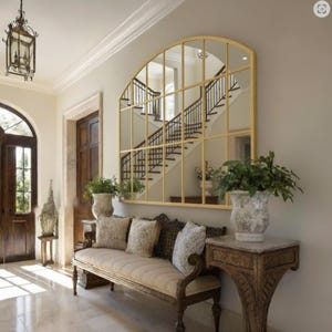 May include: An entrance hall featuring a large gold-framed mirror reflecting a staircase. A wooden bench with patterned cushions is positioned below the mirror. Decorative vases with greenery and a vintage table create a classic, elegant atmosphere.