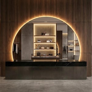 Può includere: Interno di un negozio al dettaglio di lusso con un design moderno. Lo spazio presenta pannelli in legno scuro, un grande arco illuminato e scaffali espositivi con borse e accessori. Sono visibili anche un bancone scuro e dei portabiti.