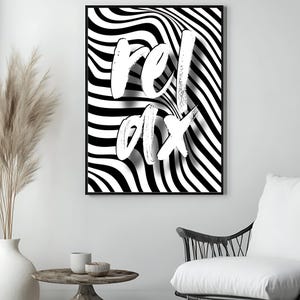 May include: Framed monochrome wall art featuring the word "relax" in white brushstrokes against a wavy, striped background. The artwork is displayed in a modern living room setting. The black frame adds a contrasting border.