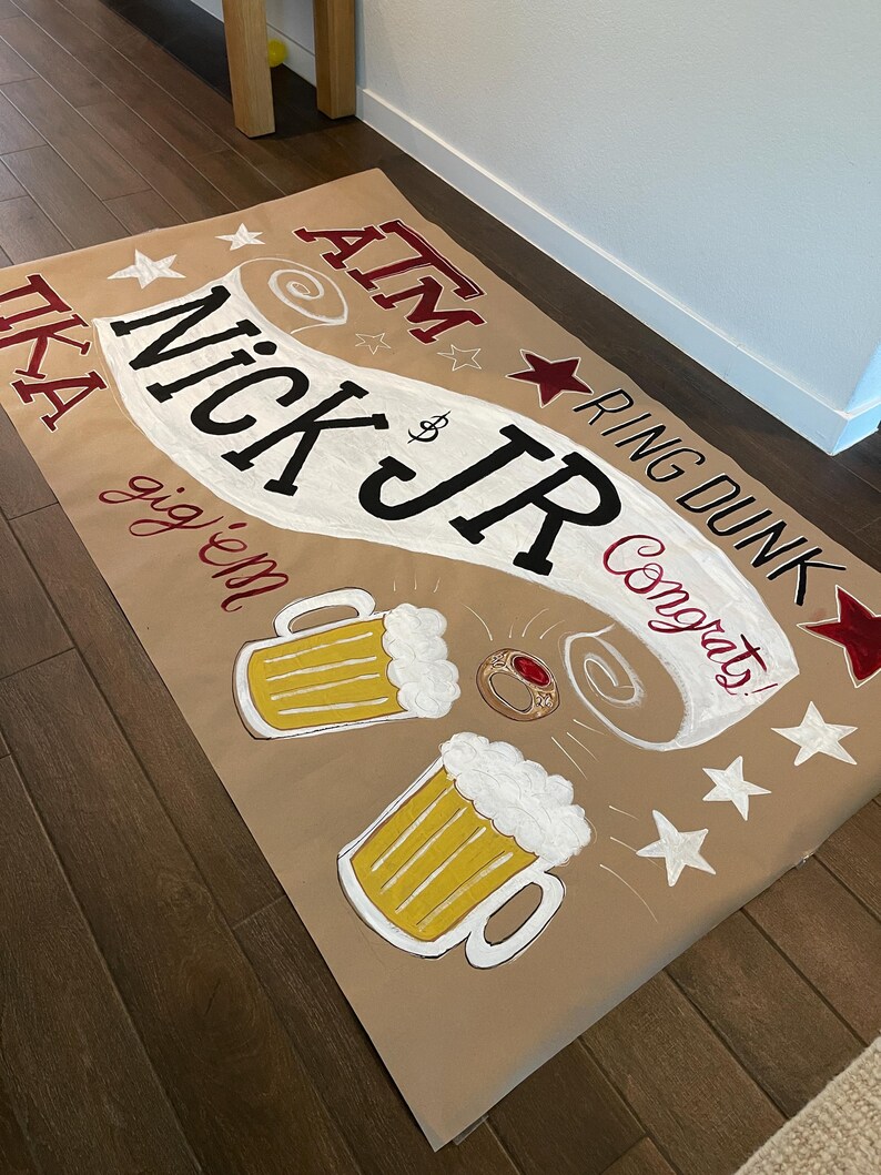 Op de afbeelding: Een bruine papieren banner met de tekst "Nick Jr" in grote zwarte letters, omringd door sterren en bierpullen. De banner bevat ook de woorden "ATM", "Ring Dunk" en "Congrats!"