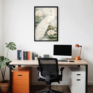 May include: A framed art print depicting a white peacock with a long tail, standing on a rock surrounded by water lilies. The artwork has a soft, light background, creating a calm and elegant feel. The frame is black.