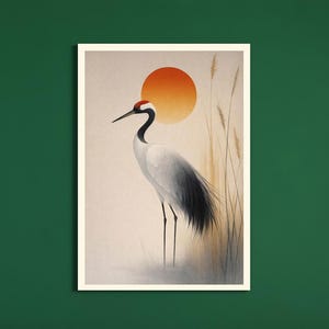 Könnte beinhalten: Ein Kunstdruck mit einem japanischen Kranich mit roter Krone, vor einer orangefarbenen Sonne. Der Kranich hat weißes und schwarzes Gefieder mit langen, schlanken Beinen. Hohe, dünne Schilfgräser befinden sich rechts vom Kranich, und der Hintergrund ist ein weiches Beige.