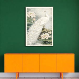 May include: A framed art print depicting a white peacock with a long tail, standing on a rock surrounded by water lilies. The artwork uses a soft watercolour style with white, green, and grey tones. The print is displayed on a green wall above an orange cabinet.