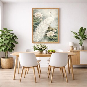 May include: A framed watercolour print featuring a white peacock with a long tail, standing on a rock surrounded by lotus flowers. The artwork has a soft, ethereal quality, with a light colour palette and a natural wood frame. The print is displayed above a wooden dining table.