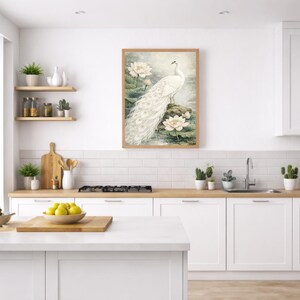May include: A framed print depicting a white peacock with a long tail, standing on a rock surrounded by water lilies. The artwork is in a soft watercolour style, with a natural, serene theme. The frame is light brown.