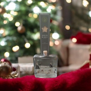 Könnte beinhalten: Eine klare Glasflasche mit einem Holzstopfen und einem Etikett mit der Aufschrift "DAYS TO BE JOLLY". Die Flasche steht vor einem verschwommenen Hintergrund aus einem Weihnachtsbaum und festlichen Dekorationen. Das Etikett zeigt einen Stern und eine Winterszene.