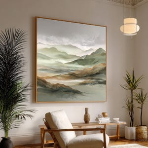 May include: Large framed landscape painting depicting a mountain range in shades of green, brown, and gray. The artwork features a hazy, atmospheric effect, with a gold-colored frame. The painting is displayed in a well-lit room with plants and furniture.