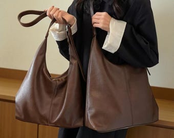 May include: Two brown leather shoulder bags. One bag has a curved handle and a crescent shape. The other bag is a larger, rectangular tote bag. Both bags are a rich, warm brown color and appear to be made of a smooth leather material.