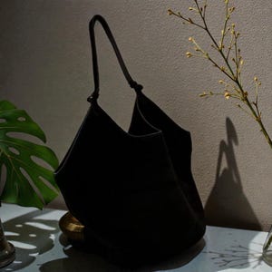 Peut inclure: Un sac fourre-tout noir avec une seule poign&eacute;e. Le sac est fait d'une mati&egrave;re souple et a une large ouverture. Le sac est pos&eacute; sur une table &agrave; c&ocirc;t&eacute; d'une plante.