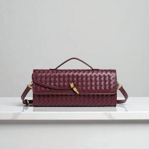 May include: A burgundy woven leather handbag with a top handle and a detachable shoulder strap. The bag features a gold-coloured clasp and hardware. The bag is rectangular and has a woven pattern.