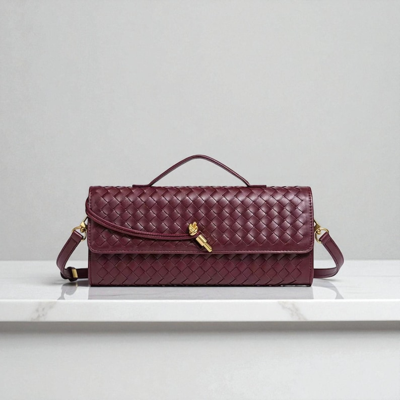 May include: A burgundy woven leather handbag with a top handle and a detachable shoulder strap. The bag features a gold-coloured clasp and hardware. The bag is rectangular and has a woven pattern.