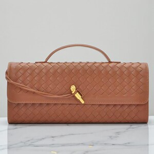 May include: A tan woven leather clutch bag with a top handle and a flap closure secured by a gold-coloured clasp. The rectangular bag has a braided pattern and a long, thin strap. The bag is made of leather.