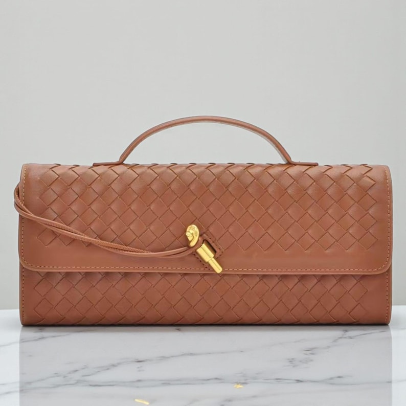 May include: A tan woven leather clutch bag with a top handle and a flap closure secured by a gold-coloured clasp. The rectangular bag has a braided pattern and a long, thin strap. The bag is made of leather.