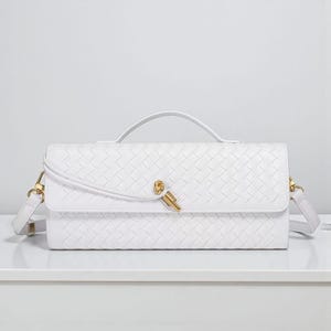 May include: A white rectangular handbag with a woven design. It has a top handle, a gold-coloured clasp, and a detachable shoulder strap. The bag is displayed on a white surface.