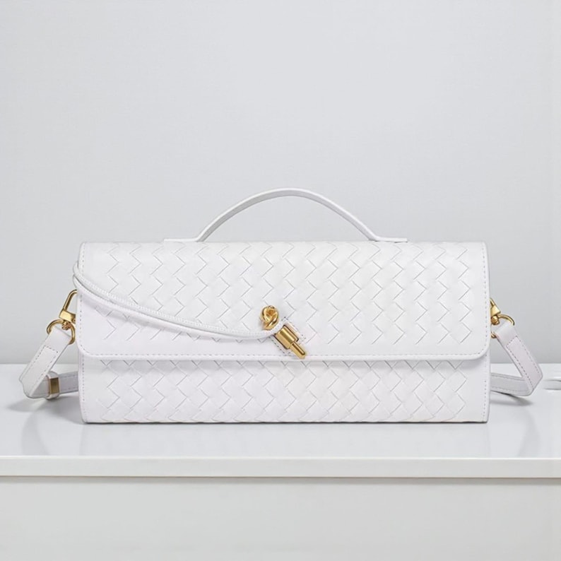 May include: A white rectangular handbag with a woven design. It has a top handle, a gold-coloured clasp, and a detachable shoulder strap. The bag is displayed on a white surface.