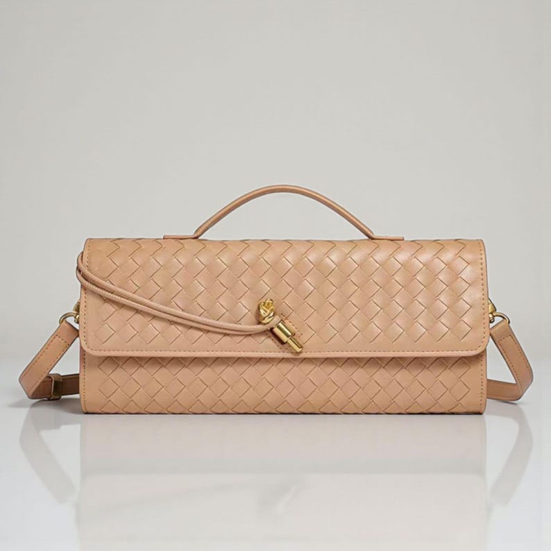 May include: A tan-coloured, rectangular handbag with a woven pattern. It features a top handle, a detachable shoulder strap, and a gold-coloured clasp. The bag is made of a soft, leather-like material.