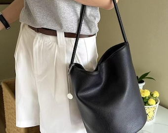 May include: Black leather bucket bag with a long strap and a silver chain detail. The bag has a textured surface and a curved top. The bag is carried over the shoulder.