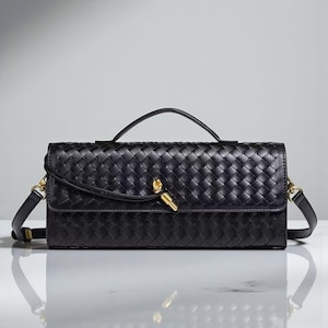 May include: A black woven leather handbag with a top handle and a detachable shoulder strap. The rectangular bag features a gold-toned clasp and hardware. The bag's design includes a woven pattern, adding texture to the accessory.