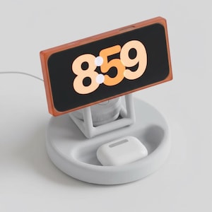 Può includere: Una stazione di ricarica bianca e grigia con un orologio digitale che mostra "8:59". L'orologio ha una cornice arancione. Una custodia bianca per auricolari wireless si trova in un'area incassata della stazione.