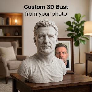 Puede incluir: Un busto 3D personalizado de un hombre, hecho a partir de una foto, se exhibe sobre una mesa de madera. El busto es gris y detallado, con una representación realista del rostro de la persona. Una foto enmarcada del mismo hombre está detrás del busto. El texto "Custom 3D Bust from your photo" está en la parte superior.