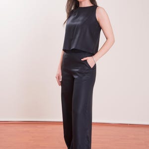May include: A sleeveless, navy blue top and matching wide-leg pants. The top has a round neckline and a cropped design. The pants feature a high waist and pockets. The outfit is made of a smooth, shiny fabric, creating a sleek, elegant look.