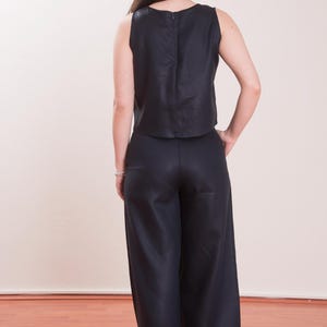 May include: A sleeveless, navy blue top and matching wide-leg pants. The top has a simple, rounded neckline and a zipper closure in the back. The pants are high-waisted and flowy, creating a sleek, monochromatic outfit.