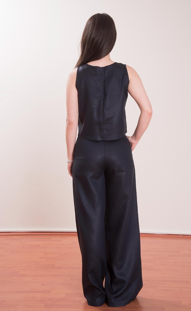 May include: A sleeveless, navy blue top and matching wide-leg pants. The top has a simple, rounded neckline and a zipper closure in the back. The pants are high-waisted and flowy, creating a sleek, monochromatic outfit.