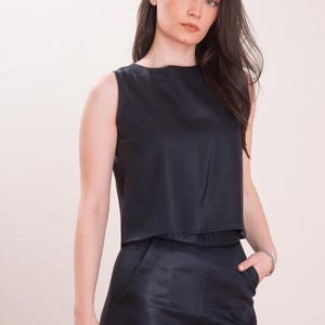 May include: Sleeveless black top and matching pants. The top has a round neckline and a cropped design. The pants have a wide leg and pockets. The outfit is made of a smooth, dark fabric.
