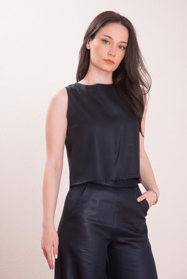 May include: Sleeveless black top and matching pants. The top has a round neckline and a cropped design. The pants have a wide leg and pockets. The outfit is made of a smooth, dark fabric.
