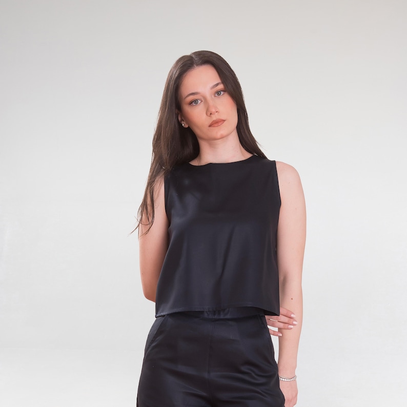 May include: A black sleeveless top and matching shorts. The top has a round neckline and a straight hem. The shorts are high-waisted. The fabric appears to be a smooth, shiny material, possibly satin or silk. The outfit is a solid black color.