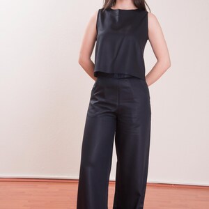May include: A sleeveless, navy blue top and matching wide-leg pants. The top has a simple, square neckline. The pants are long and flowing. The outfit is made of a smooth, possibly satin-like fabric. The model is standing in front of a plain wall.