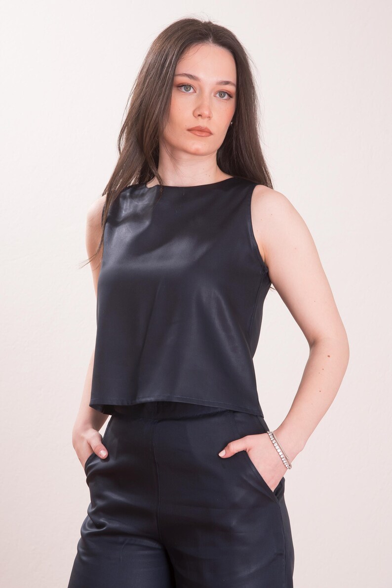 May include: Sleeveless navy blue top and matching pants. The top has a round neckline and a smooth, satin-like texture. The pants have pockets. The outfit is a solid color and appears to be made of a lightweight material.