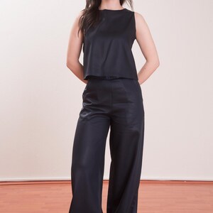 May include: A sleeveless, navy blue top and matching wide-leg pants. The outfit has a sleek, satin-like appearance. The model is standing in front of a plain background and wooden floor.