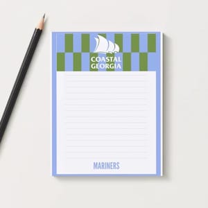 May include: A lined notepad with a blue and green checkered top border and the words "Coastal Georgia" and "Mariners" printed on it. A black pencil with a gold ferrule rests beside the notepad.