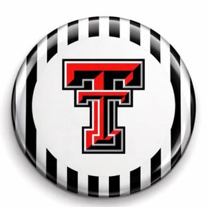 May include: A round button with a white center featuring a red and black letter "T". The button has a black and white striped border. The design is a logo, likely for a team or organization.