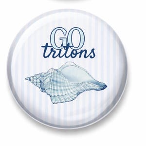 Puede incluir: Un botón redondo blanco con un fondo a rayas azules y blancas. Presenta una ilustración detallada de una concha marina y las palabras "GO tritons" en escritura azul. Acabado brillante.