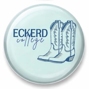 Puede incluir: Un botón azul claro con las palabras "ECKERD college" en azul marino. Dos botas de vaquero azul marino aparecen en el botón. El botón tiene un acabado brillante y un fondo azul claro.