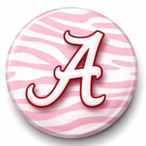 May include: A round button with a pink and white zebra stripe pattern background. A white letter "A" with a red outline is centered on the button. The letter has a serif font.
