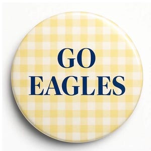May include: A round button with a yellow and white gingham pattern. The words "GO EAGLES" are printed in navy blue, centered on the button. The button has a glossy finish and a white background.