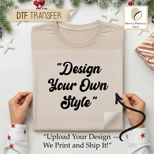 May include: A beige t-shirt with the text "Design Your Own Style" in black script. The phrase "Upload Your Design - We Print and Ship It!" is also visible. The shirt is being held by two hands.