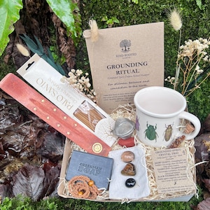 May include: A gift box with a grounding ritual theme. It contains a mug with insect illustrations, Palo Santo incense, a soap bar, crystals, and a tea infuser. The box includes a card that reads "GROUNDING RITUAL".
