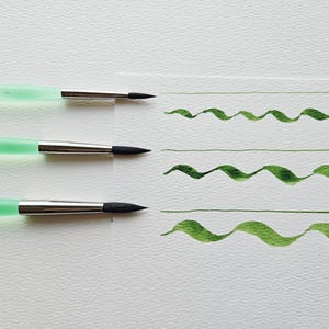 May include: Three watercolour paint brushes with mint green handles and silver ferrules. Each brush has a black tip and is shown creating a straight line and a wavy line of green paint on white paper. Art supplies.