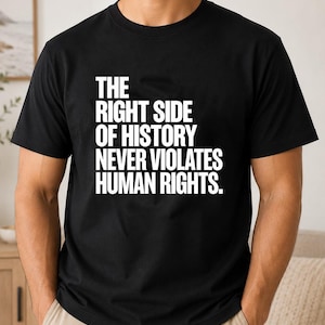 May include: A black short-sleeved t-shirt featuring white text printed on the chest that reads: THE RIGHT SIDE OF HISTORY NEVER VIOLATES HUMAN RIGHTS. The garment has a crew neckline and a standard fit, constructed from a solid black fabric.