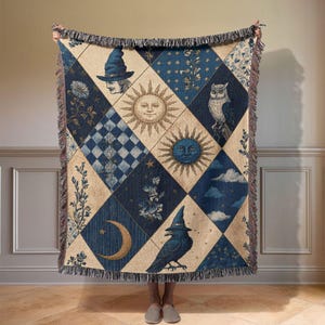 May include: A woven throw blanket featuring a diamond-patterned design in shades of navy blue and cream. The pattern includes illustrations of a wizard, suns, a crescent moon, an owl, a raven, clouds, stars, and floral motifs with fringed edges.