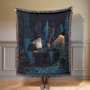 Peut inclure: Une couverture tissée représentant un magicien dans une scène nocturne. Le magicien, portant un chapeau et une robe, est assis dans un fauteuil bleu, utilisant un ordinateur portable. Un chat noir est à proximité. L'arrière-plan montre une ligne d'horizon urbaine et une lampe brillante.