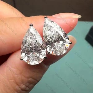 May include: A pair of pear-cut diamond earrings. The diamonds are clear and sparkling, reflecting light. The earrings are set in silver metal. The image is of jewellery.
