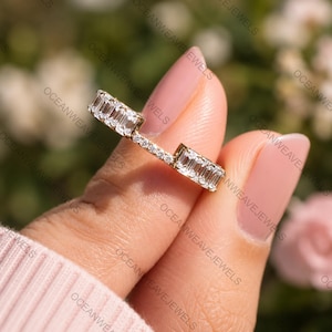 Peut inclure: Une bague en or composée de deux sections rectangulaires de pierres claires taille baguette, reliées par une fine bande de petites pierres rondes serties pavé. Le design crée un espace ouvert entre les deux groupes de pierres principales.