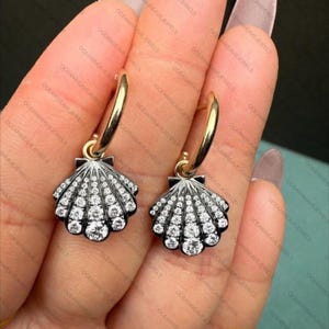 May include: A pair of gold hoop earrings with a seashell pendant. The pendants are black and silver with white gemstones. The earrings are a classic and elegant design.