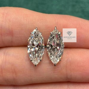 以下が含まれることがあります： マーキス型のダイヤモンドスタッドピアス。ダイヤモンドはシルバーの金属にセットされ、ニュートラルな背景に表示されています。ピアスはOceanweave Jewelsのものです。